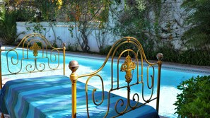 Zona junto a la piscina con estructura metálica de cama y cubierta azul a rayas.