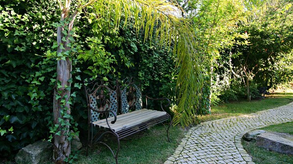 A garden with a metal bench, a cobblestone path, and lush greenery. - Uma Casa à Beira Sol (Lagos)