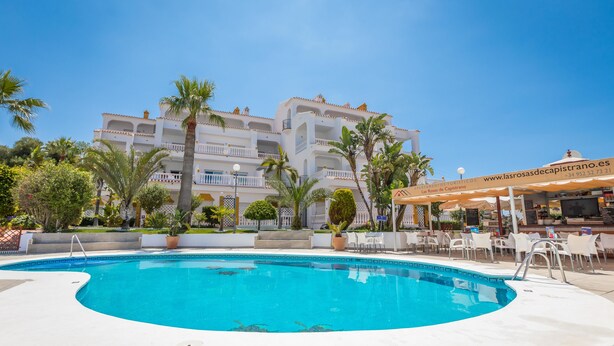 Een hotel met een zwembad, terras en palmbomen.