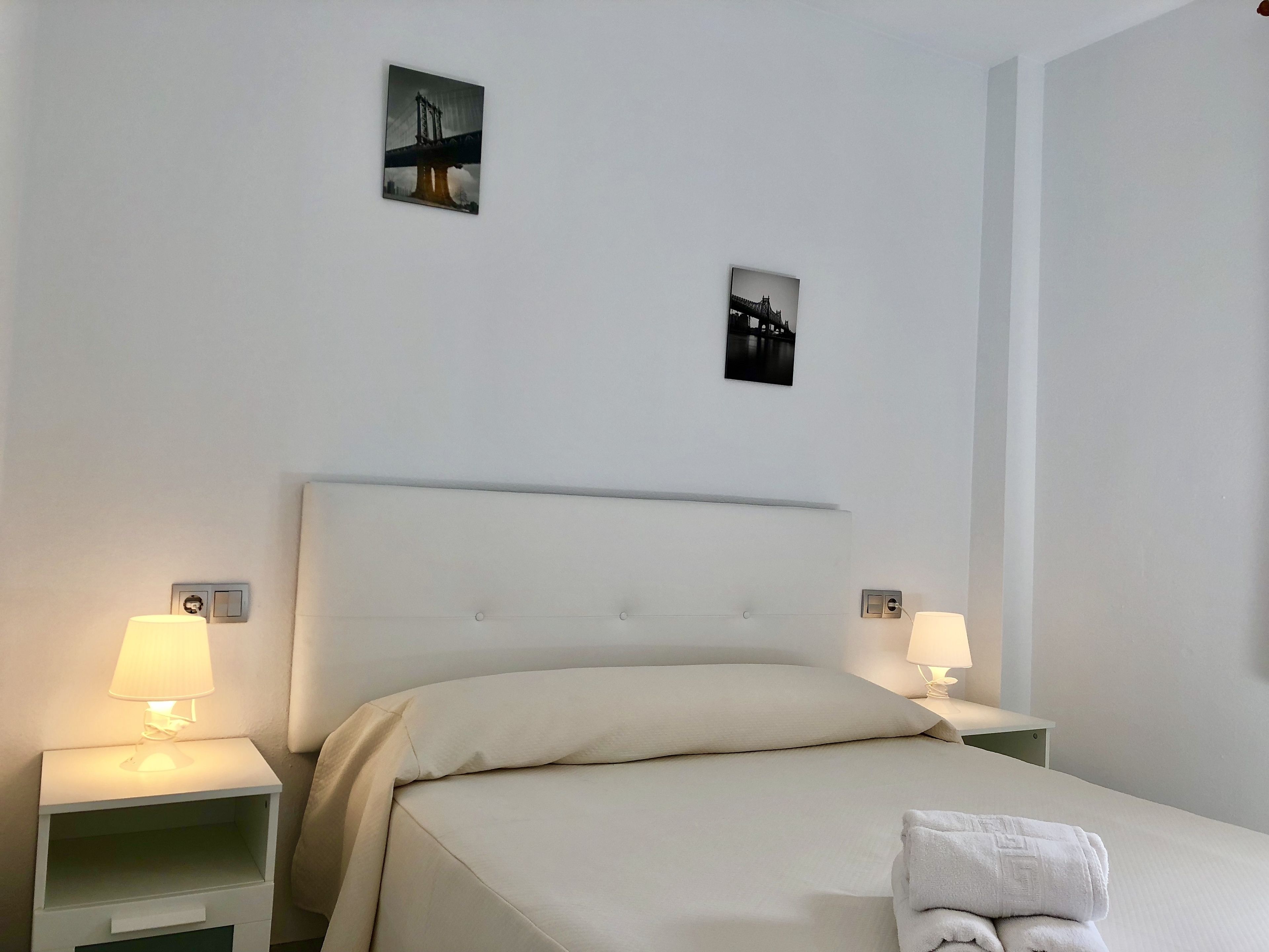 Een hotelkamer met een bed, twee nachtkastjes met lampen en twee kleine wanddecoraties.