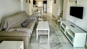 Een moderne woonkamer met een bank, salontafel en tv-meubel. In de achtergrond is een keuken zichtbaar.