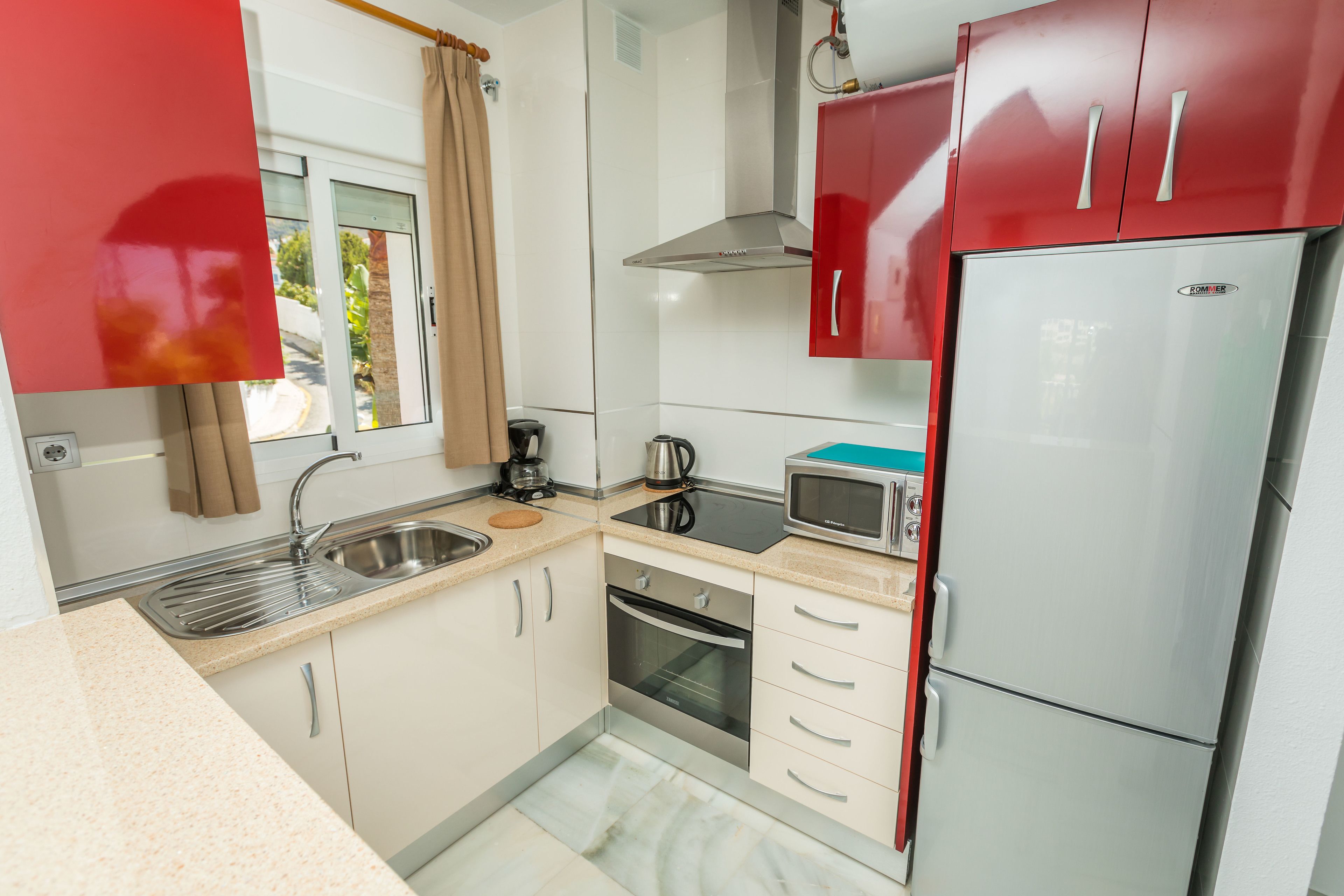 A compact kitchen with a stainless steel sink, a microwave, a built-in oven, and a refrigerator.