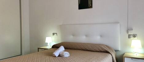 Habitación de hotel con cama, dos mesitas de noche con lámparas, un cuadro colgado en la pared y una puerta.