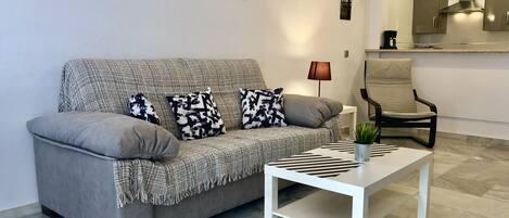 A modern living room with a grey sofa, black and white patterned cushions, a white coffee table, and a lamp.