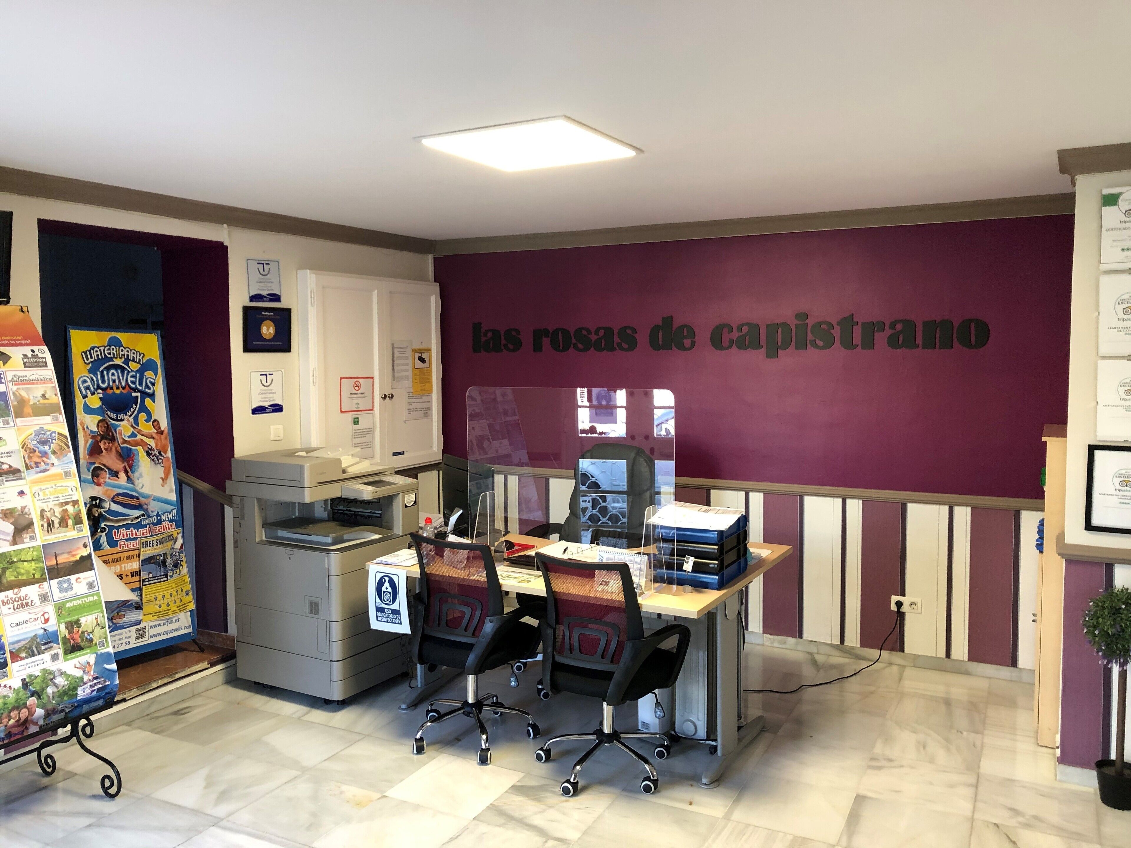 Een kantoor met een bureau, stoelen, een printer en een muur met tekst.