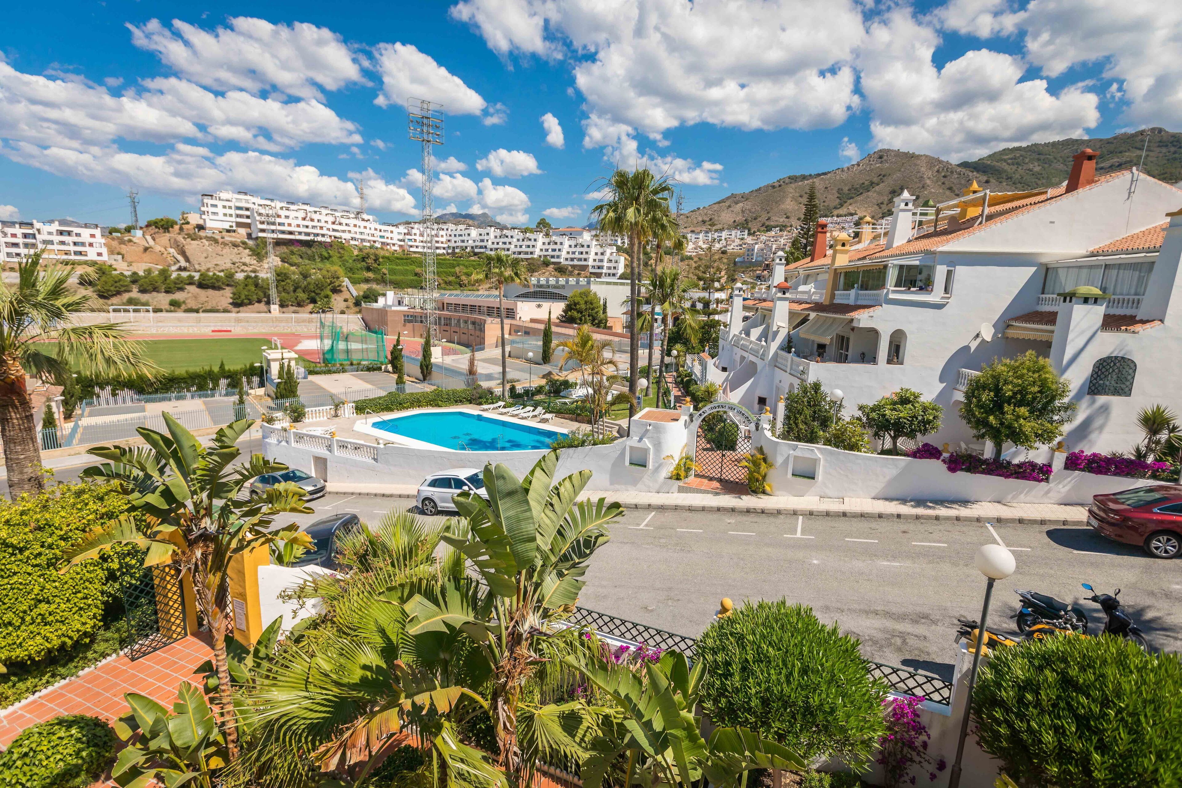 A residential area with a swimming pool, palm trees, and a view of a mountainous landscape.