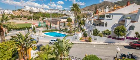 A residential area with a swimming pool, palm trees, and a view of a mountainous landscape.