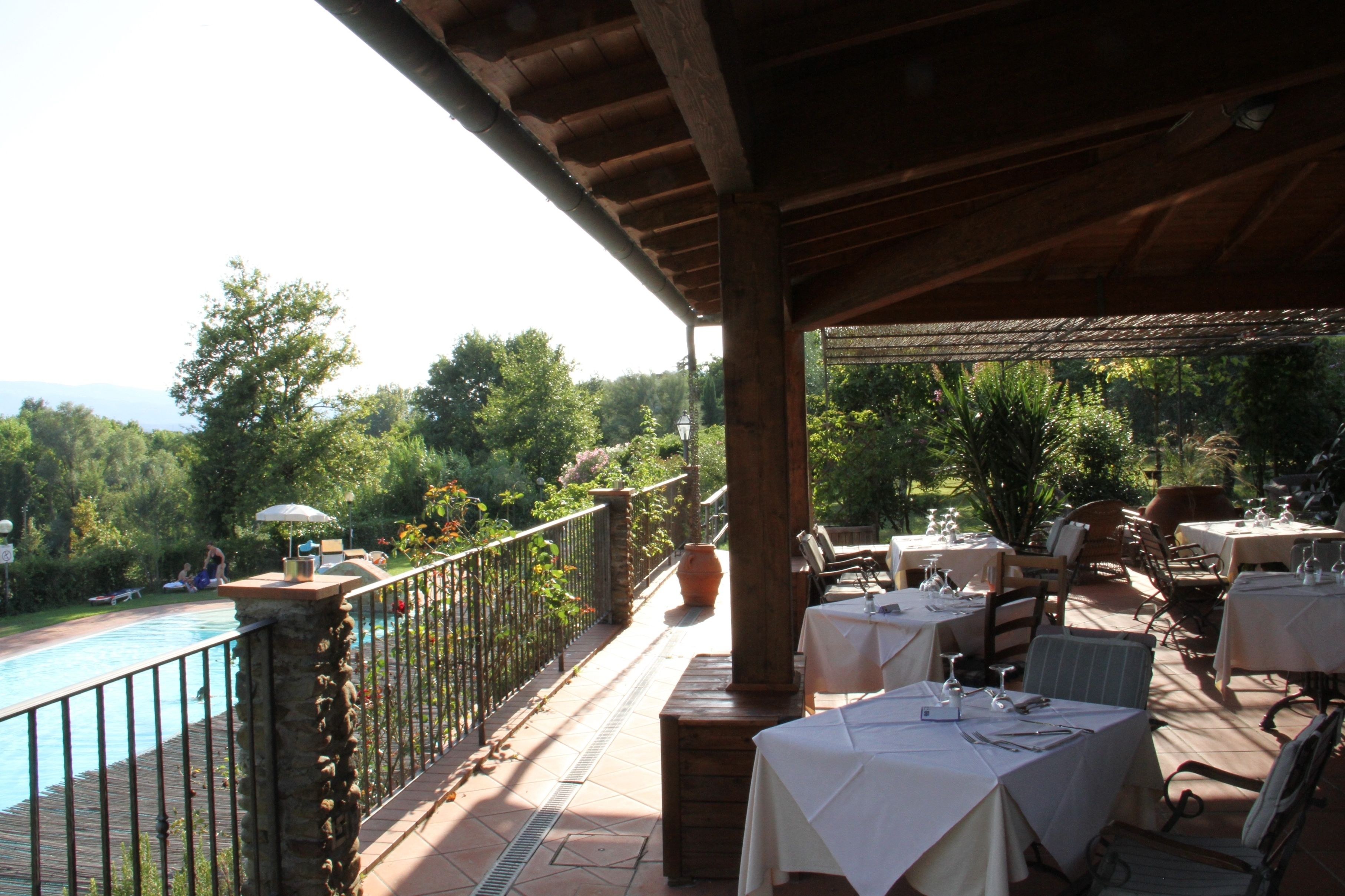 An outdoor patio with tables set for dining, a pool, and a view of the surrounding greenery.