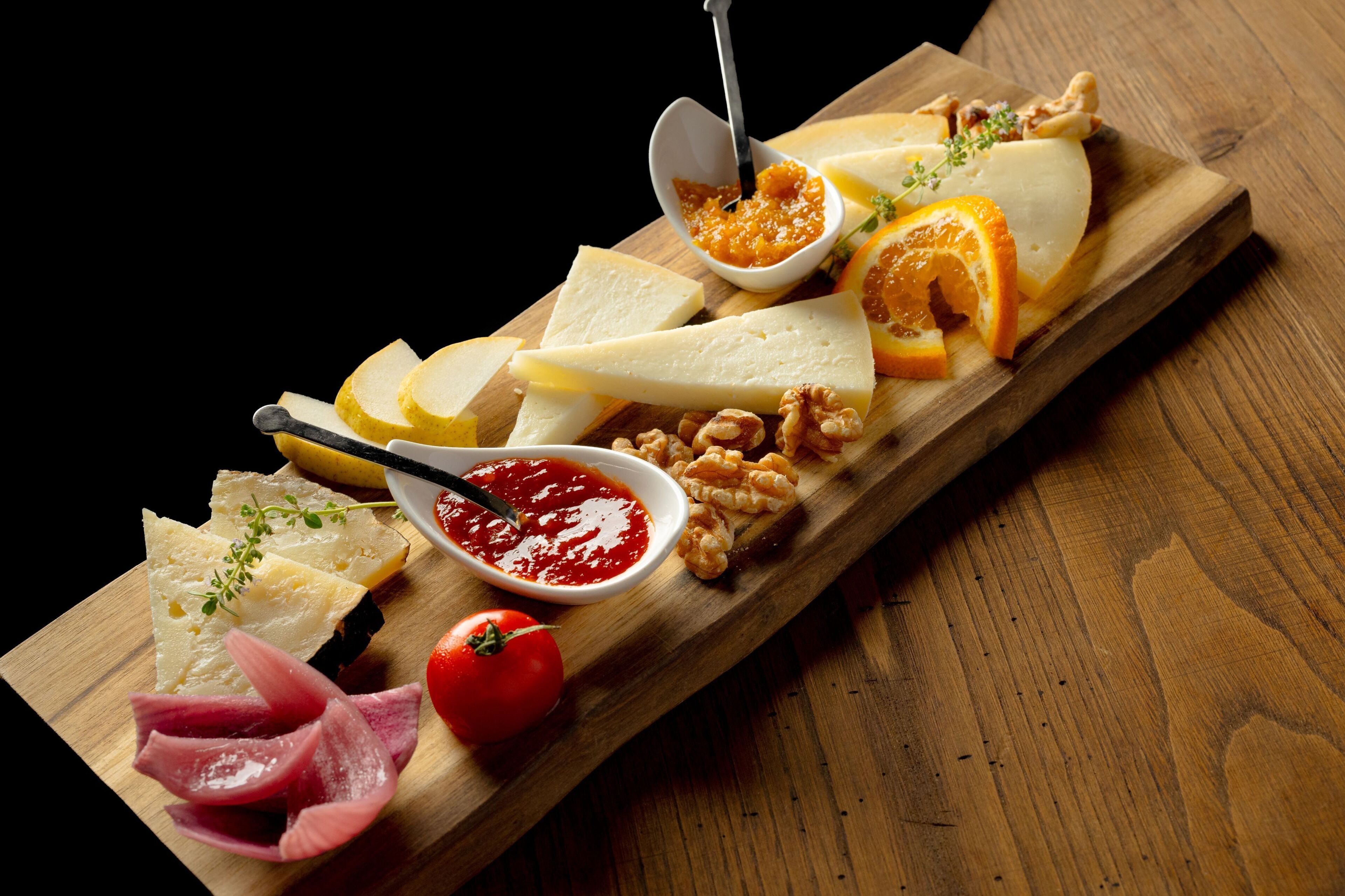 Ein Holzbrett mit verschiedenen Käsesorten, Nüssen und einer Tomate.