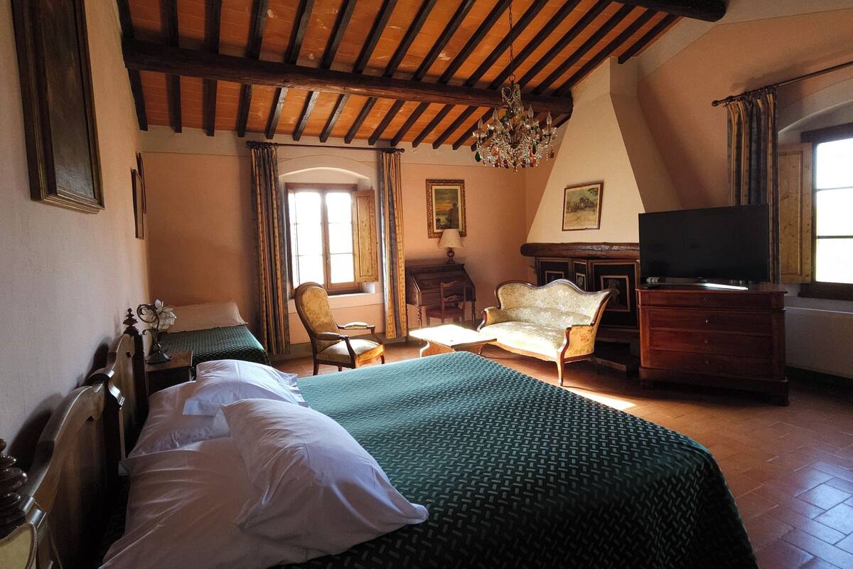 A bedroom with a wooden ceiling, a bed with a green bedspread, a chair, a dresser, and a television.