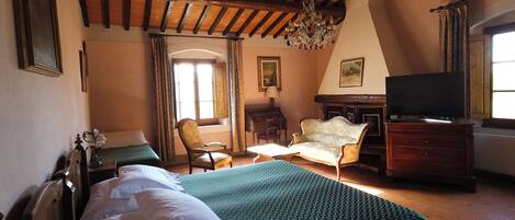 Un dormitorio con techo de madera, una cama con colcha verde, una silla, un aparador y un televisor.