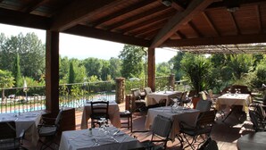 An outdoor restaurant with tables set for dining, overlooking a swimming pool and lush greenery. - Villa Rigacci (Reggello)