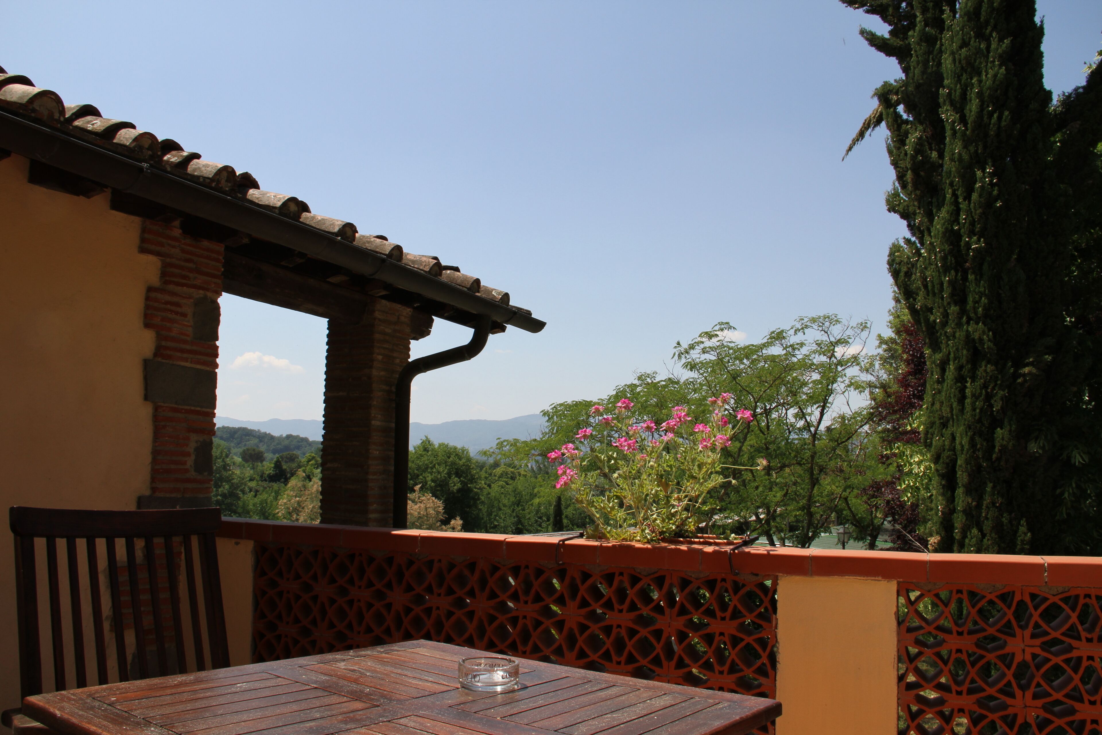 A patio with a wooden table and chairs, a brick wall, and a view of greenery and mountains.