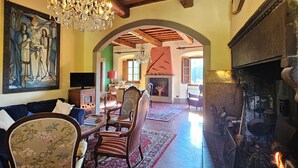 A spacious living room with a fireplace, wooden beams, a chandelier, and a large painting. - Villa Rigacci (Reggello)