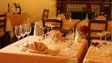 A dining area with tables set for a meal, featuring wine glasses, cutlery, and a vase with a red rose.