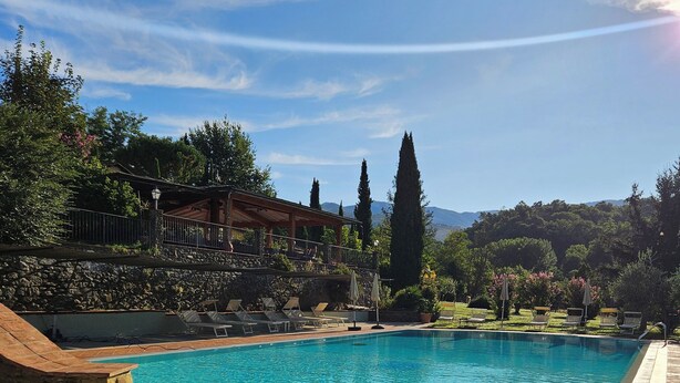 A swimming pool with a stone border, surrounded by lounge chairs and a stone wall. - Villa Rigacci (Reggello)