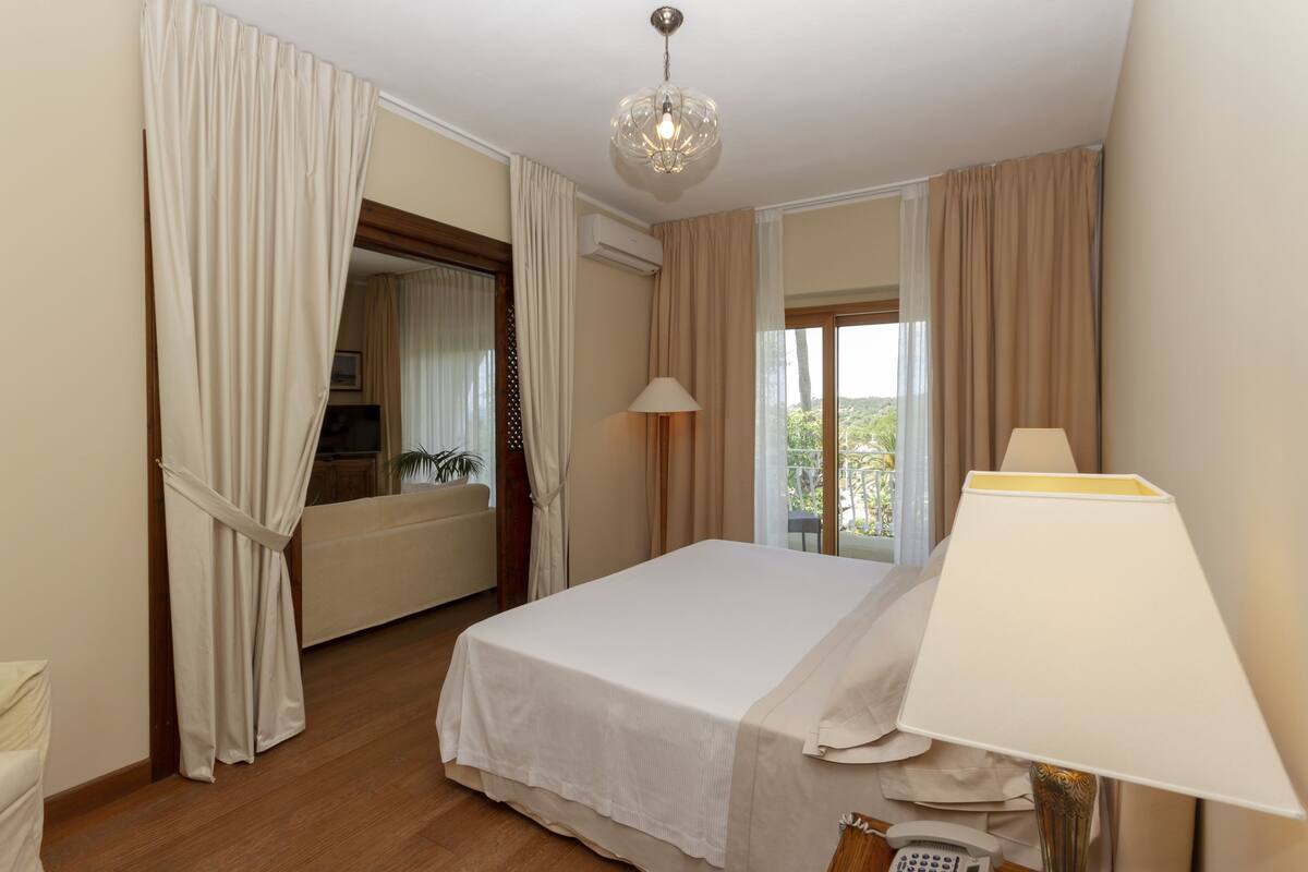 A hotel room with a bed, a lamp, a telephone, and a view of the outdoors.