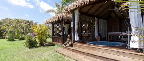 Una terraza de madera con un jacuzzi, una zona de estar cubierta y una estatua.
