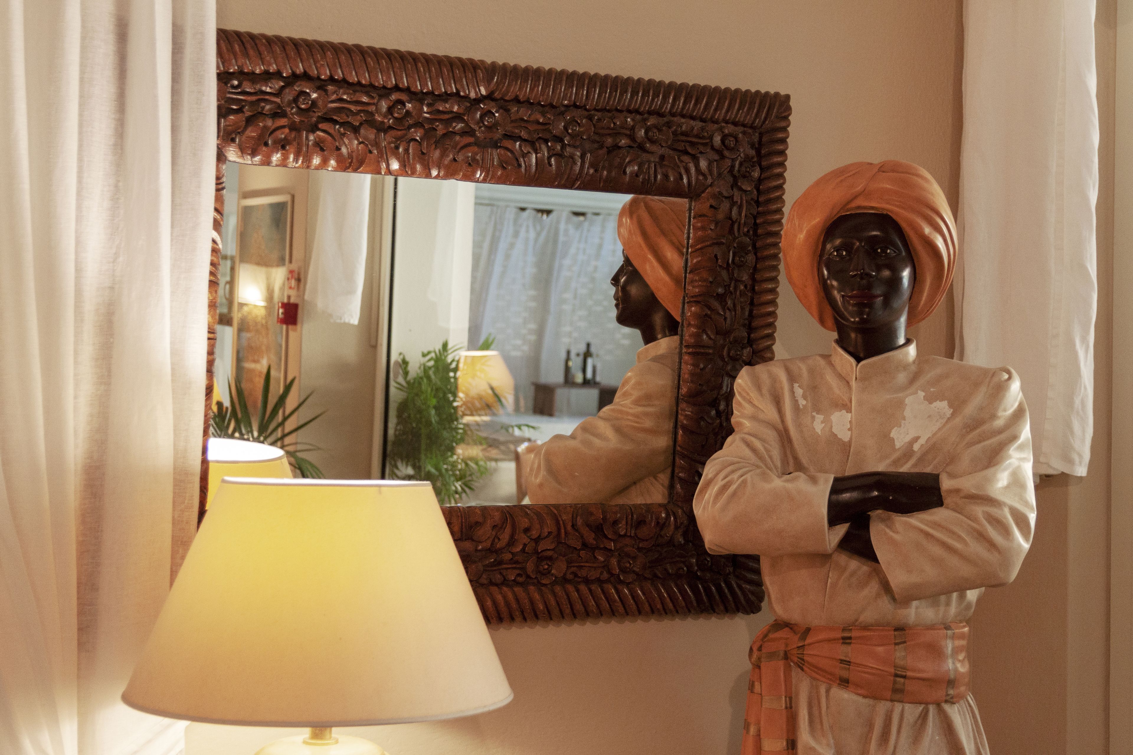 Un mannequin vêtu d’un costume traditionnel, coiffé d’un turban, se tient devant un miroir orné d’un cadre travaillé.