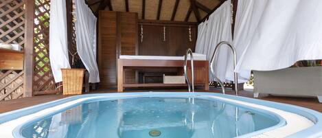 A hot tub with a wooden deck, a wooden bench, and a wicker basket.