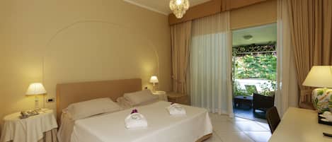 Habitación de hotel con una cama grande, dos mesitas de noche con lámparas, un escritorio con una silla y vistas al exterior a través de una puerta de cristal.