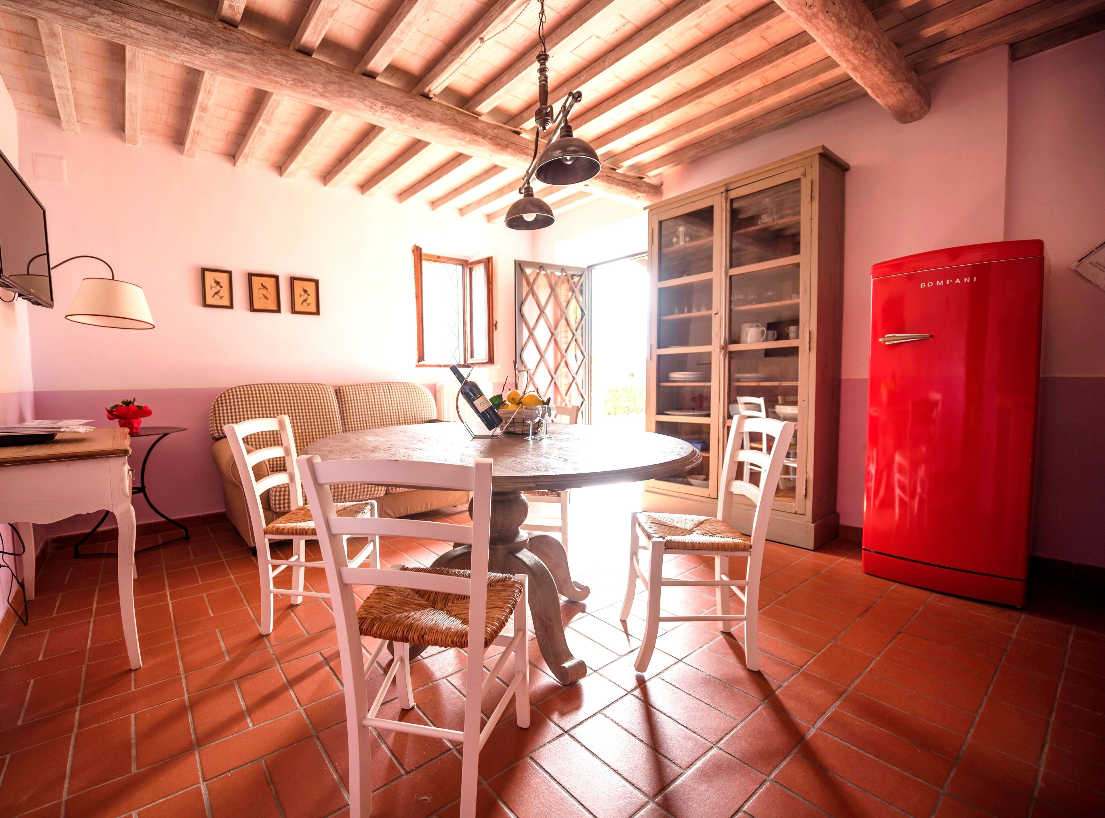A dining area with a round table, white chairs, a red refrigerator, and a wooden ceiling.