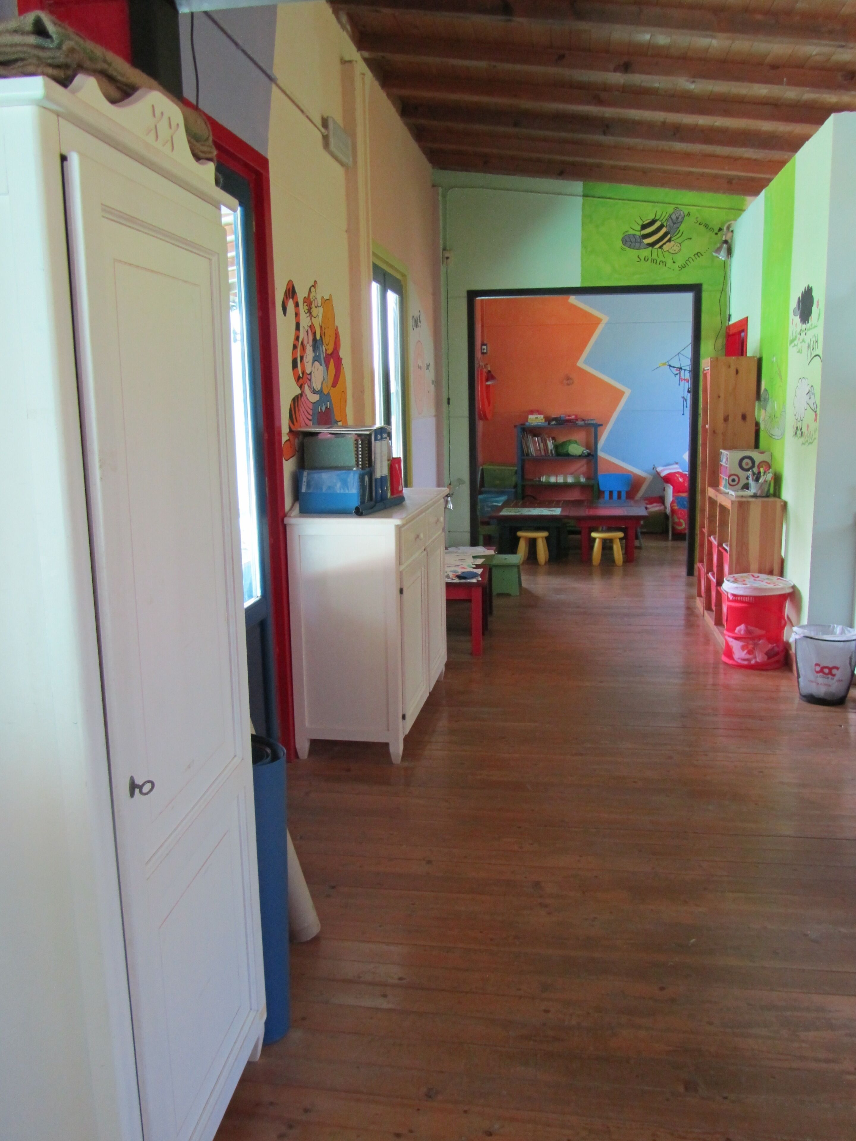Ein Zimmer mit Holzboden, einem weißen Kleiderschrank, einer roten Tür, einem Tisch mit Stühlen und einer farbenfrohen Wand mit Zickzackmuster.