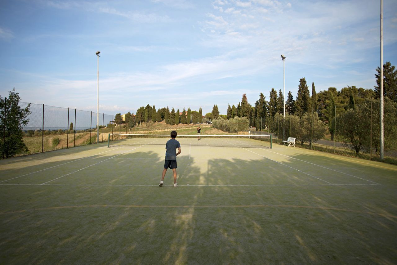 Un court de tennis avec un filet, entouré d’arbres et d’une clôture.