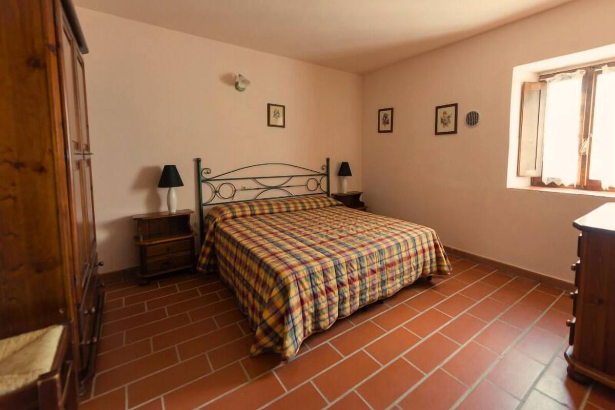 Une chambre à coucher comprenant un lit, deux tables de chevet, une armoire en bois et une fenêtre avec des rideaux.