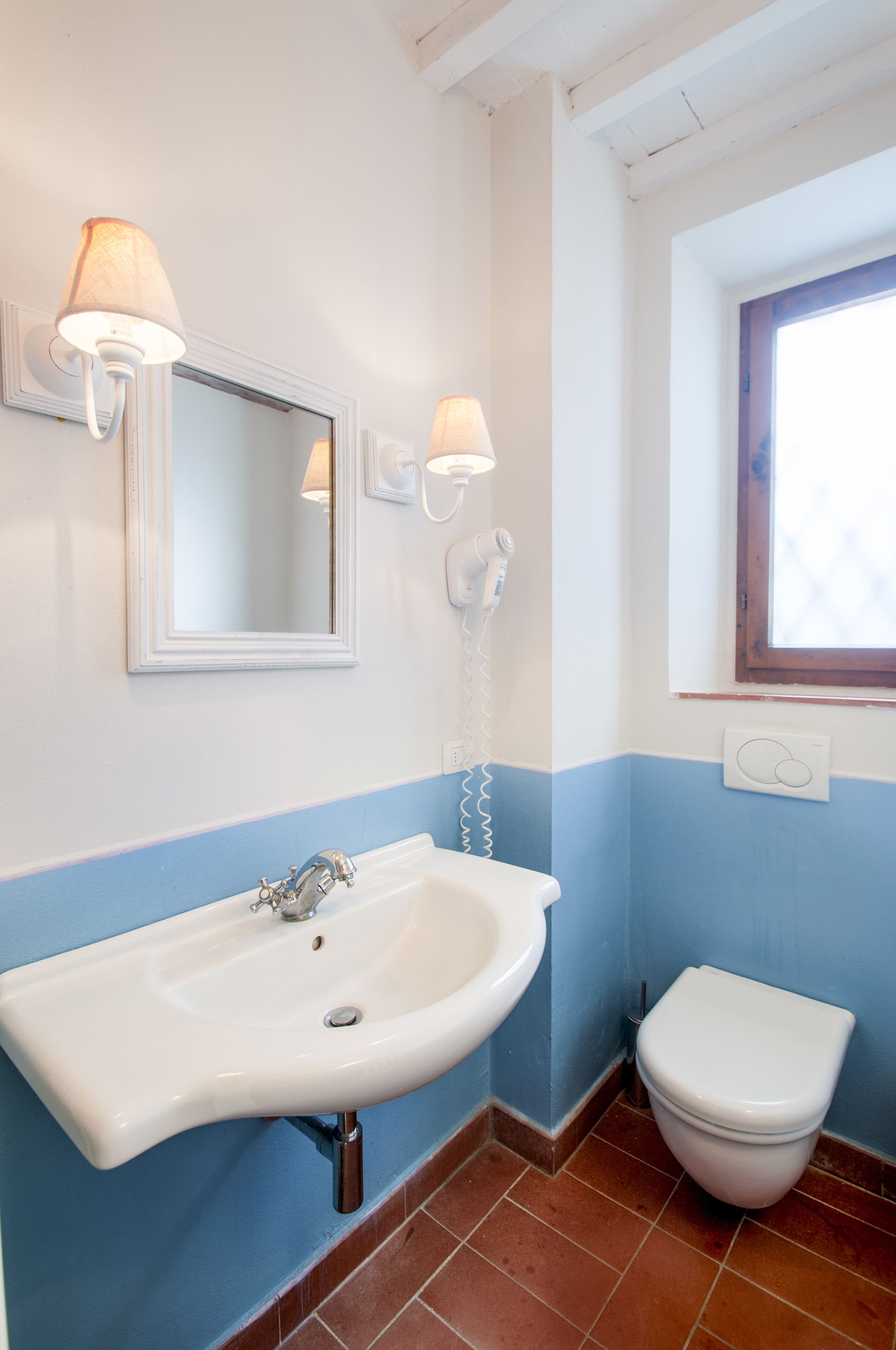 Een badkamer met een witte wastafel, een spiegel, een wit toilet en een raam.