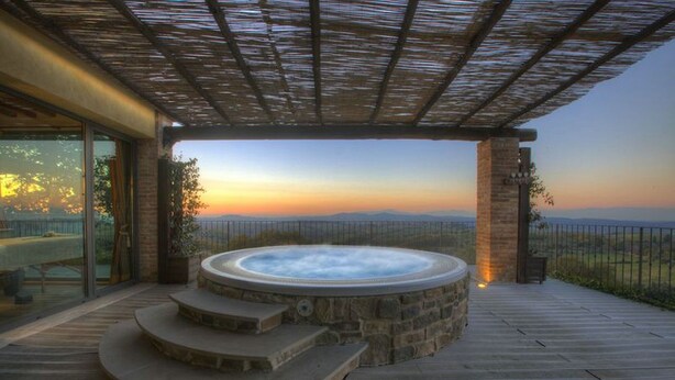 Een hottub met stenen treden die erheen leiden, onder een pergola, met uitzicht op verre heuvels.