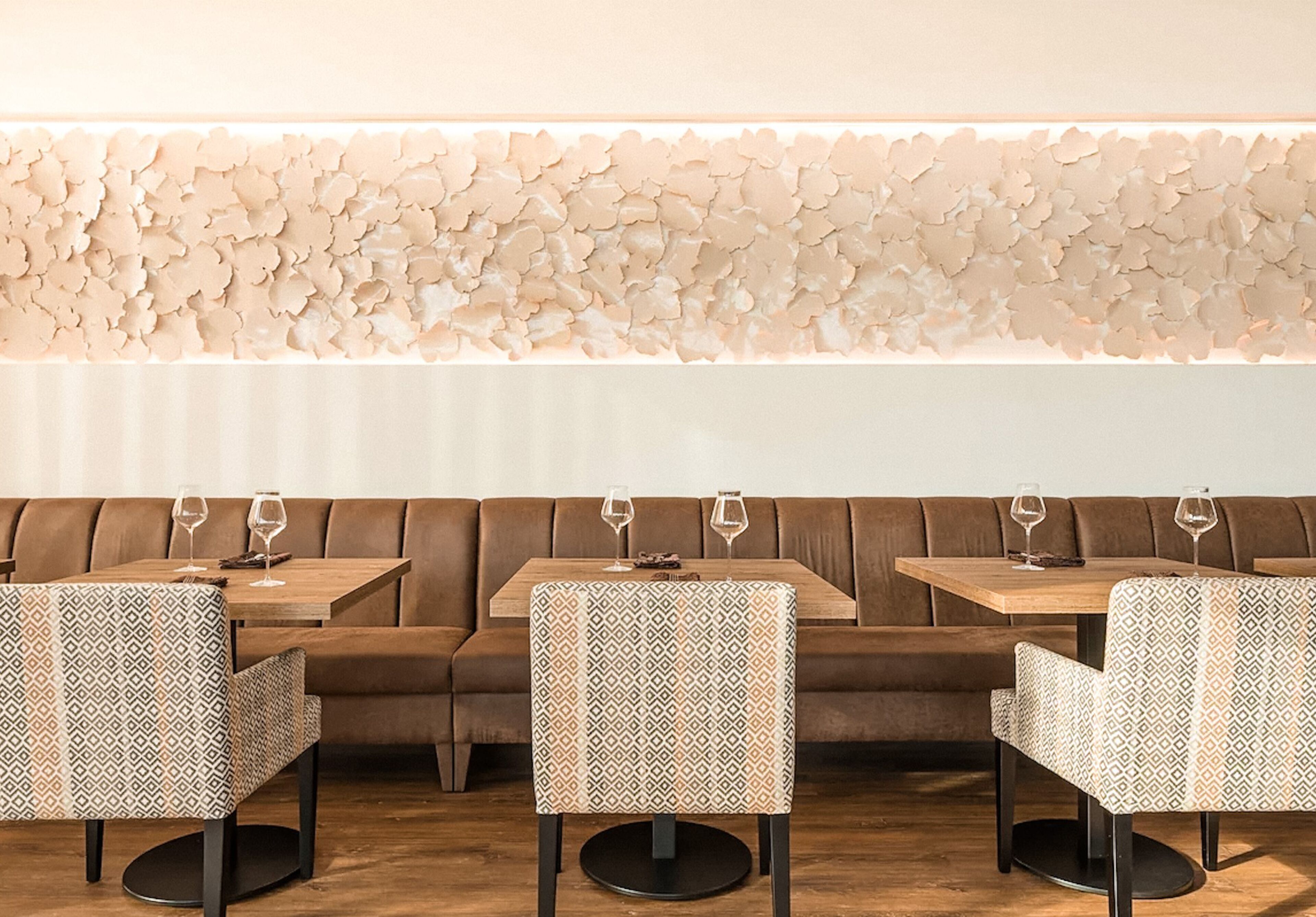 Ein Restaurantinnenraum mit gemustertem Tischlein, braunen Ledersitzbänken und einer Wand mit blattartigen Verzierungen.