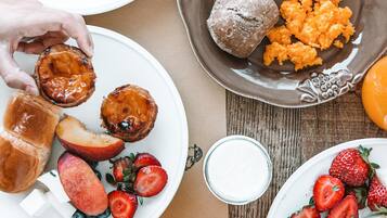 Una mesa de madera con bollos, pasteles, frutas y un vaso de zumo de naranja para el desayuno.