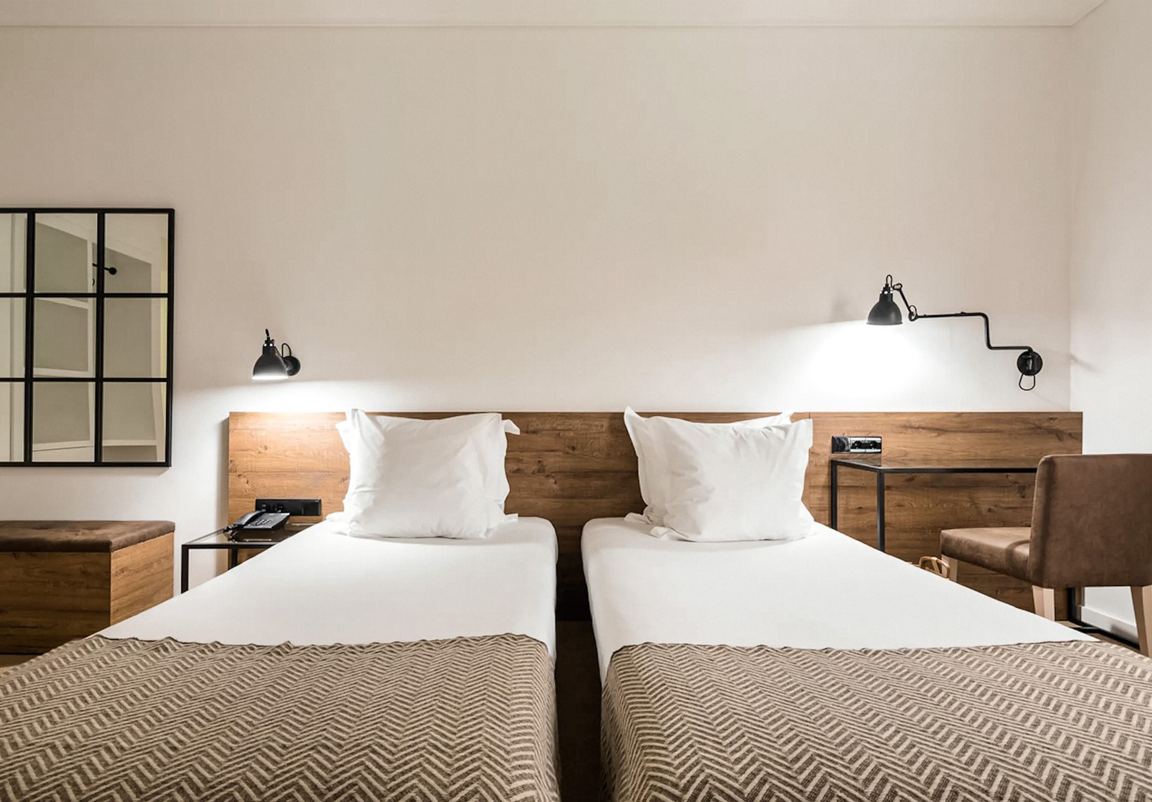 A hotel room with two single beds, a wooden headboard, a desk with a lamp, and a chair.