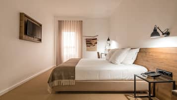A hotel room with a bed, a bedside table with a lamp, a TV mounted on the wall, and a window with curtains.