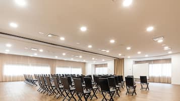 A spacious conference room with rows of foldable chairs, a large whiteboard, and a projector screen.