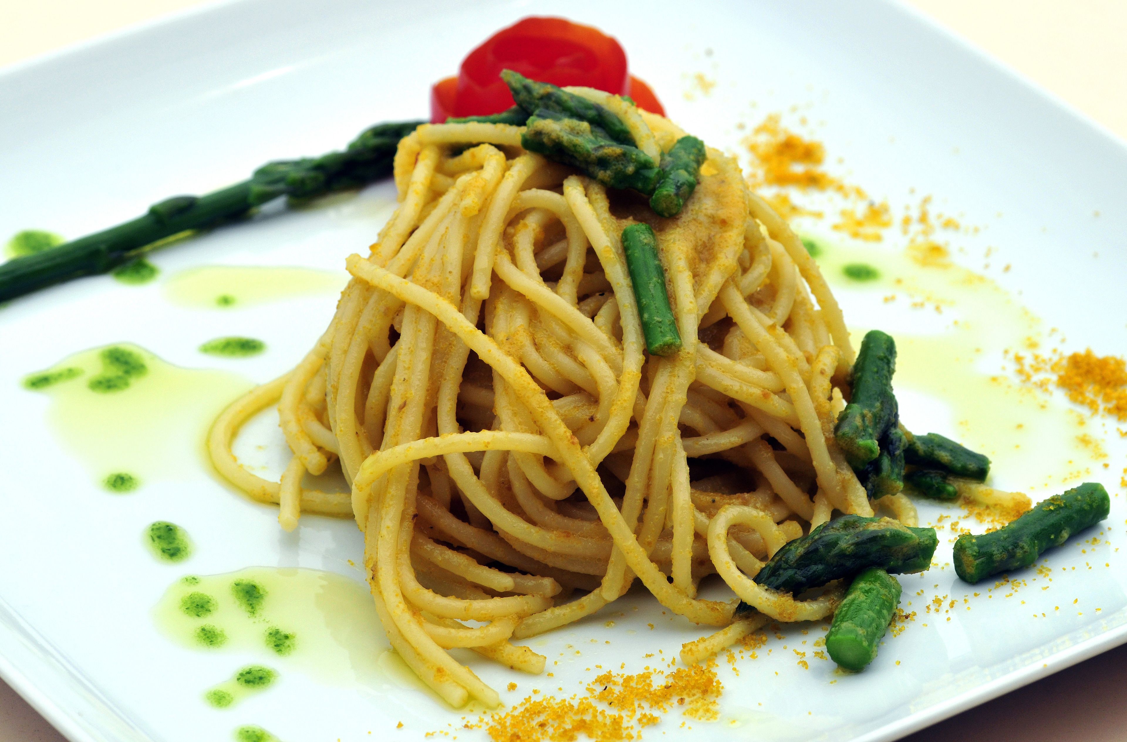 A plate of spaghetti with green asparagus and a red pepper.