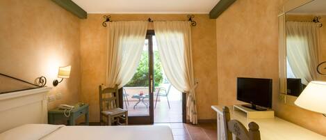 Habitación de hotel con cama, escritorio con televisor, una silla, una mesita con teléfono y ventana con cortinas.