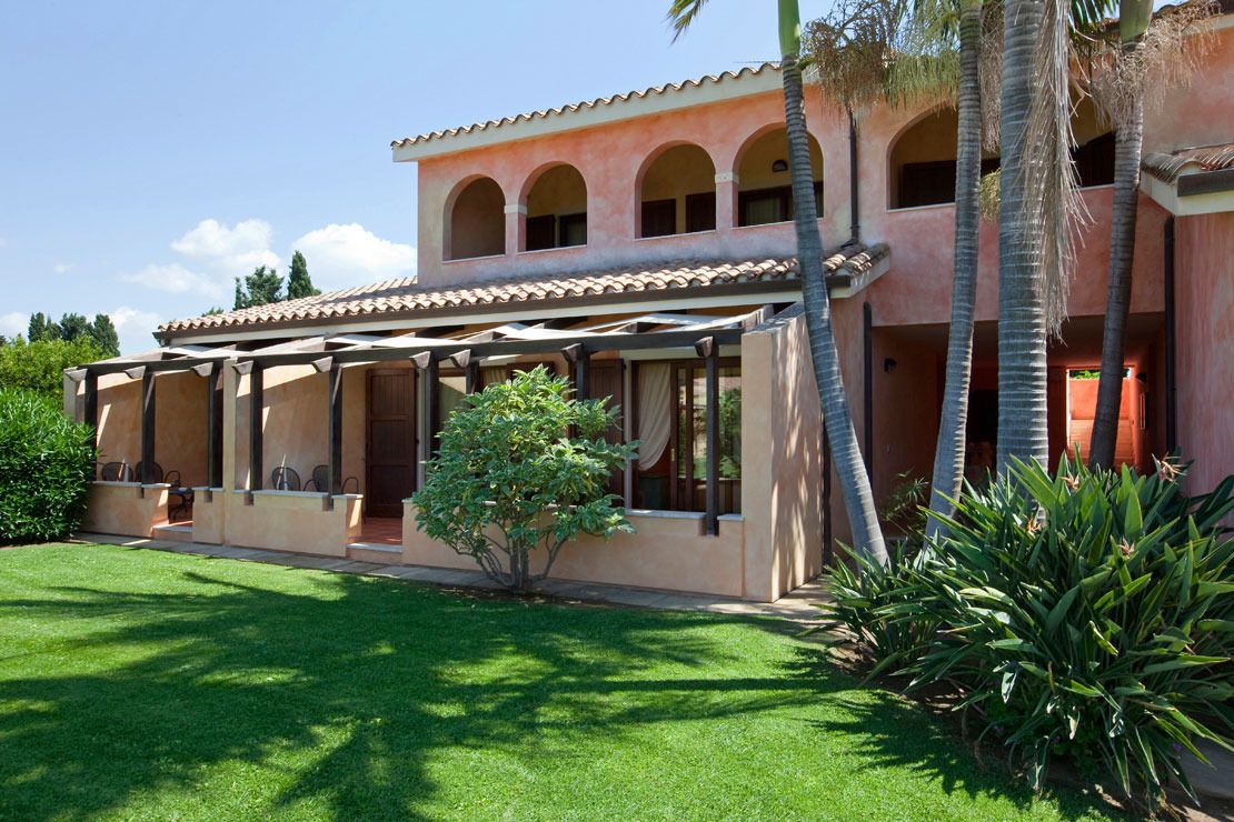 A two-story building with a covered patio area, palm trees, and a well-maintained lawn.