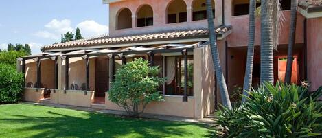 A two-story building with a covered patio area, palm trees, and a well-maintained lawn.