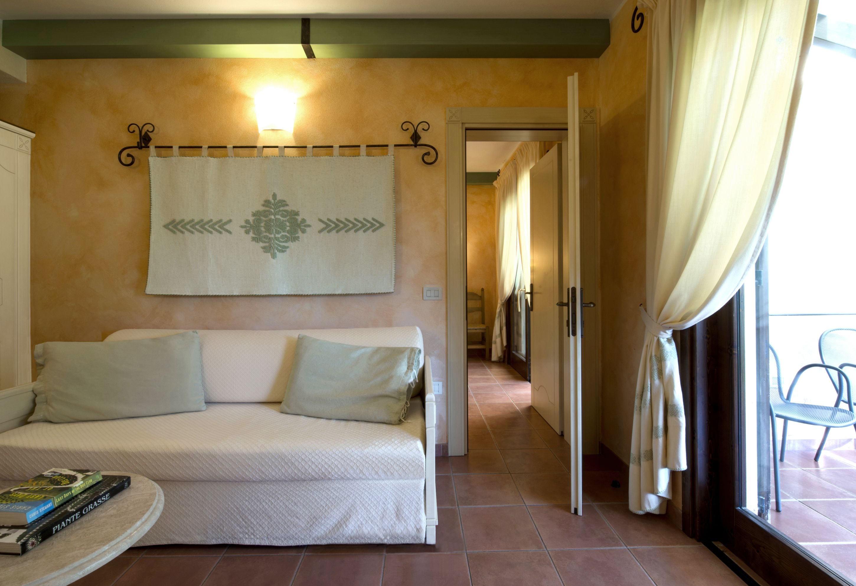 A room with a white sofa, a wall tapestry, and a view through a glass door.