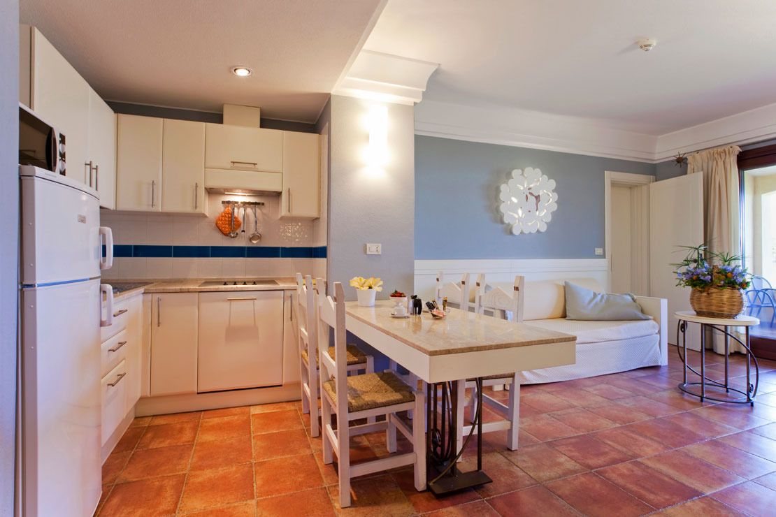 A modern kitchen with white cabinets, a dining table with chairs, and a living area with a sofa and a decorative wall piece.