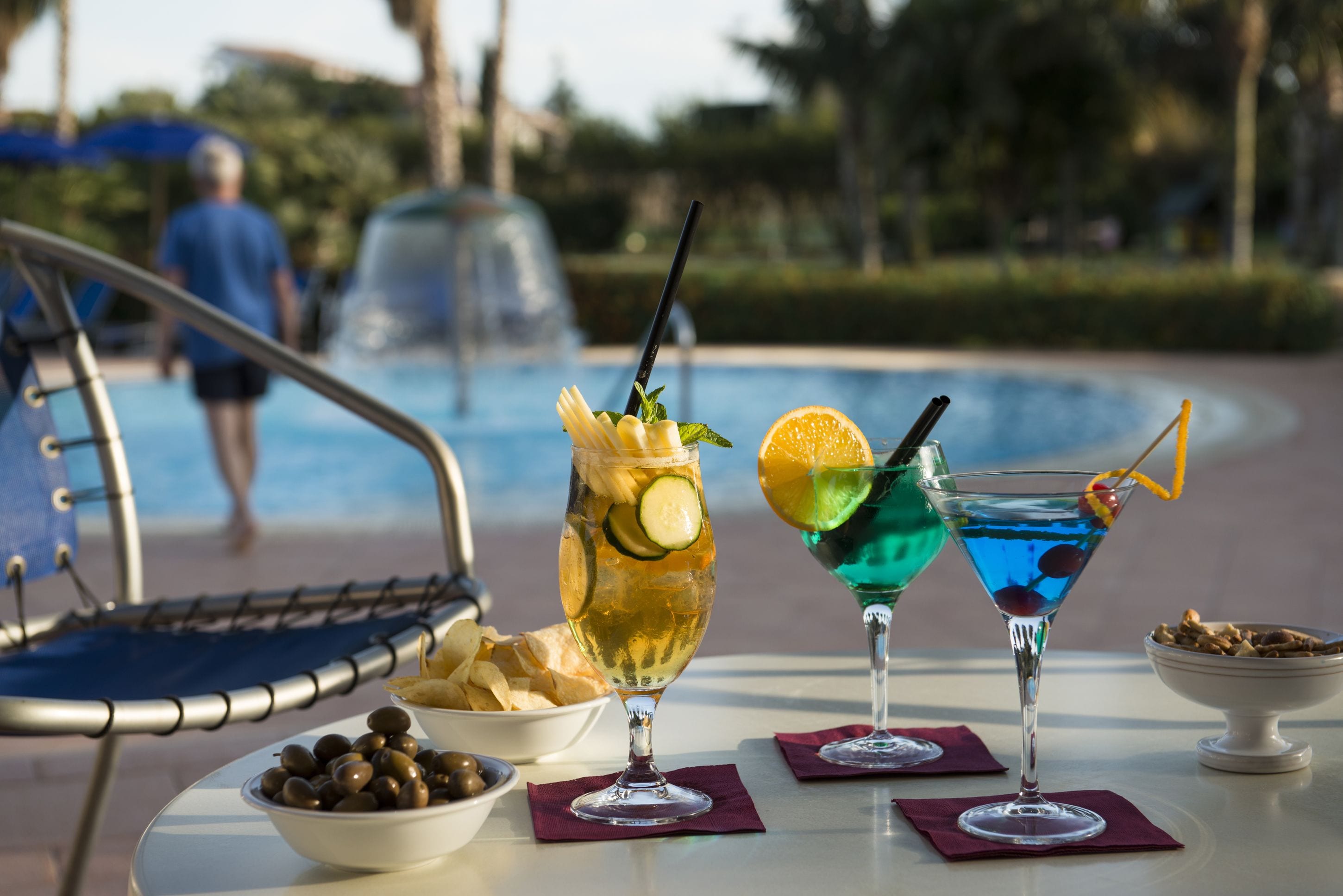 A poolside table with two cocktails, a bowl of olives, and a chair.
