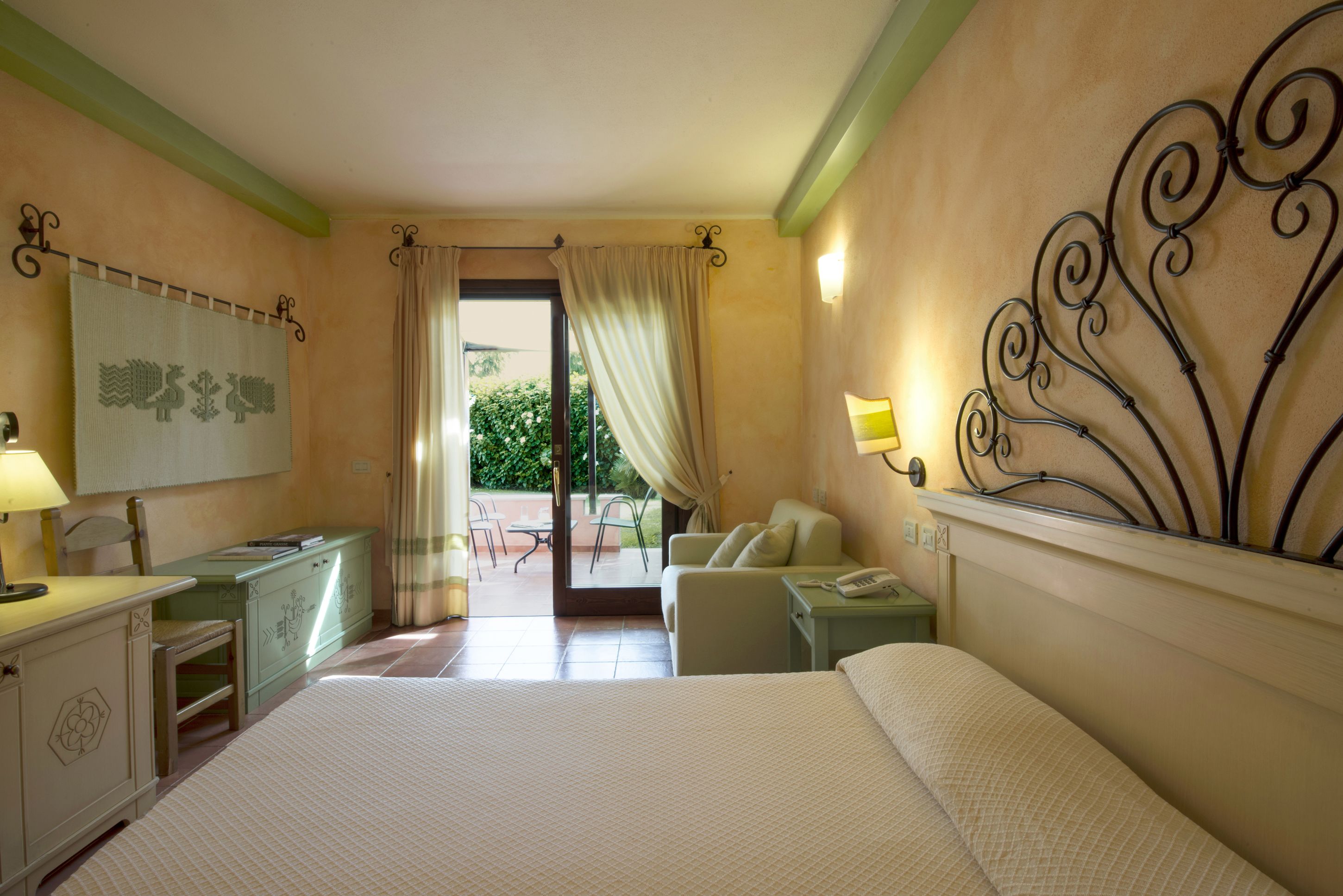 Habitación de hotel con cama, escritorio, silla, pequeña mesa, mesita de noche y vistas al exterior.