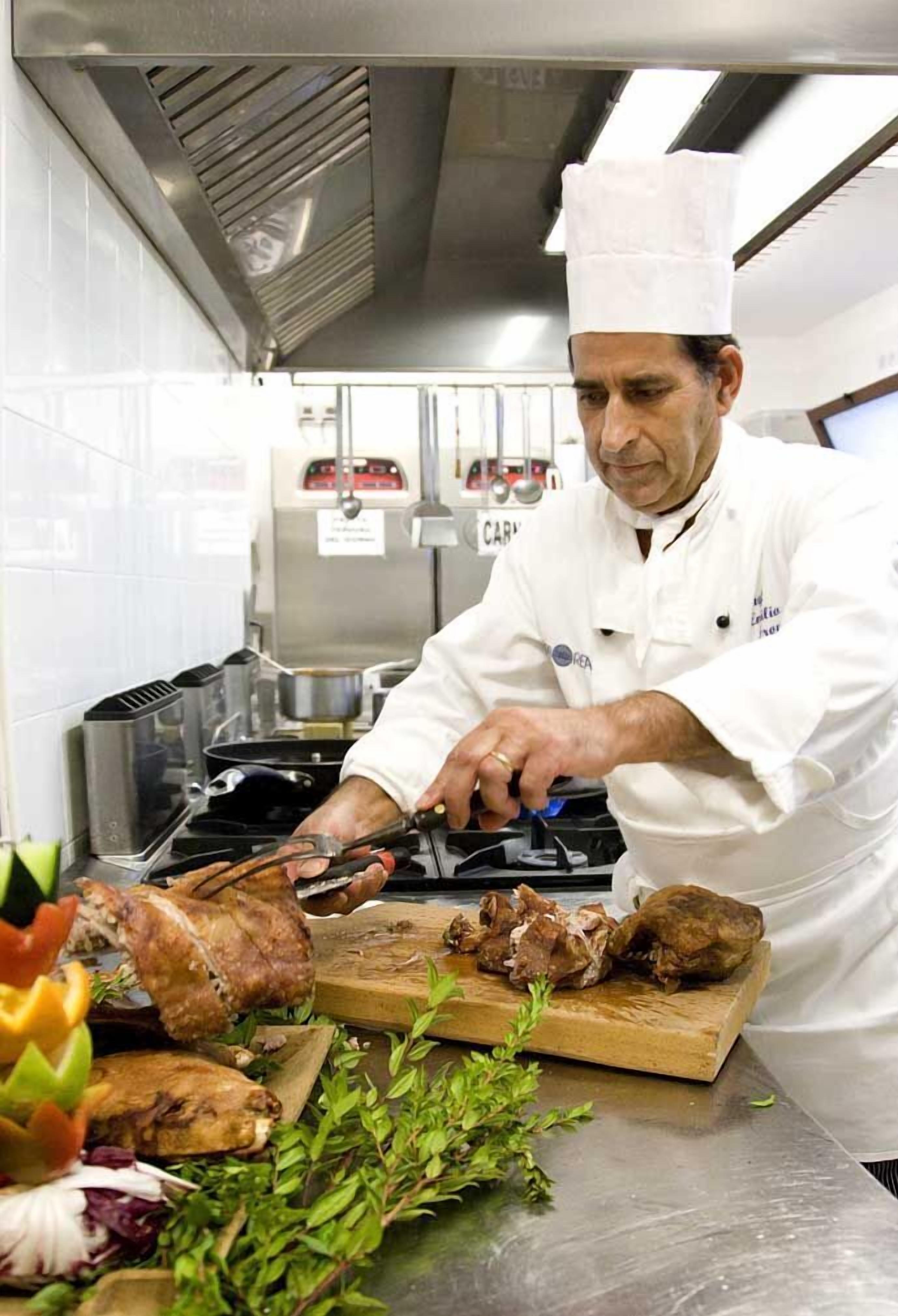 A chef in a professional kitchen with stainless steel appliances, a cutting board with meat, and various kitchen utensils.