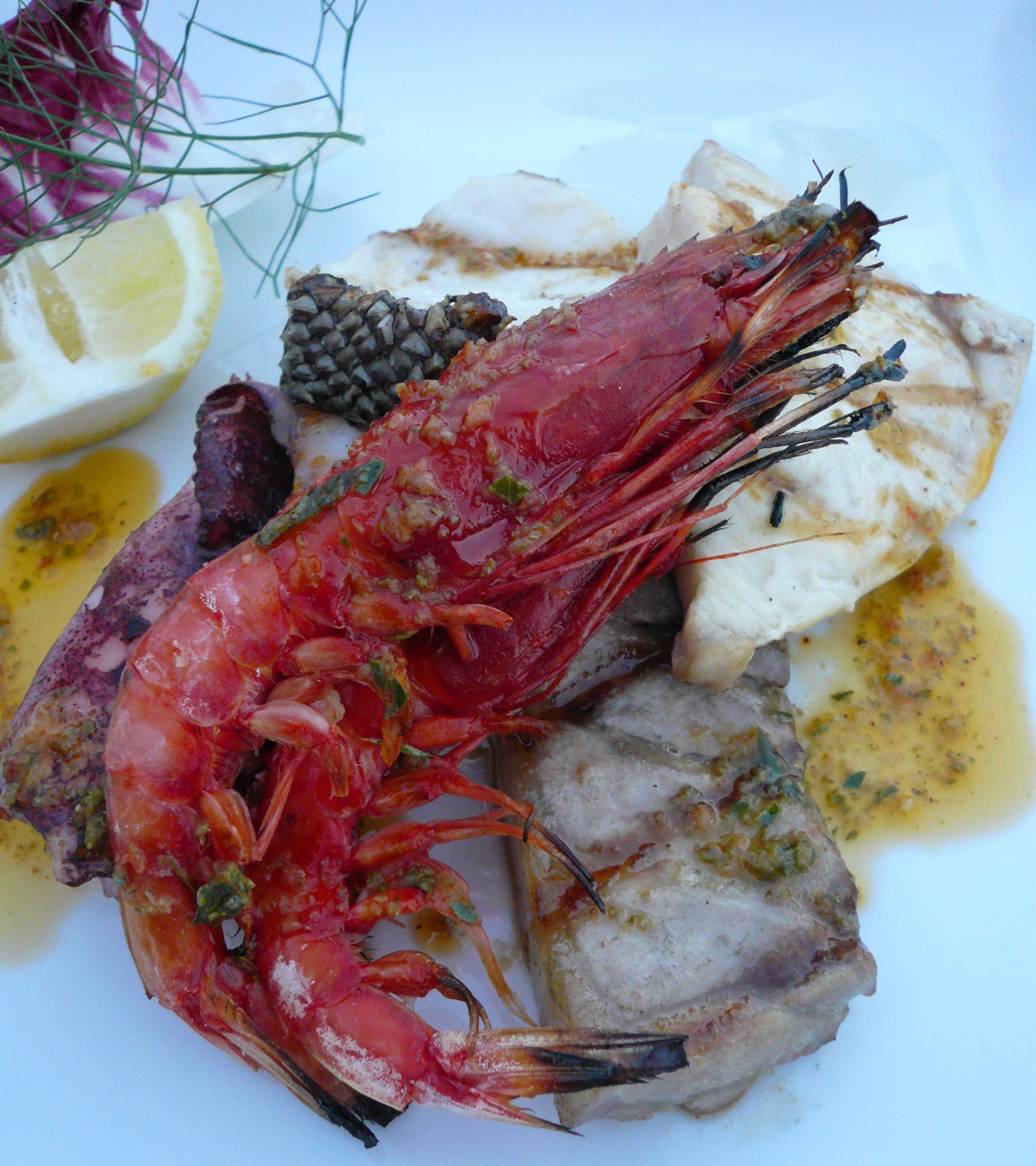 A plate with a cooked shrimp, fish, lemon, and a pine cone.