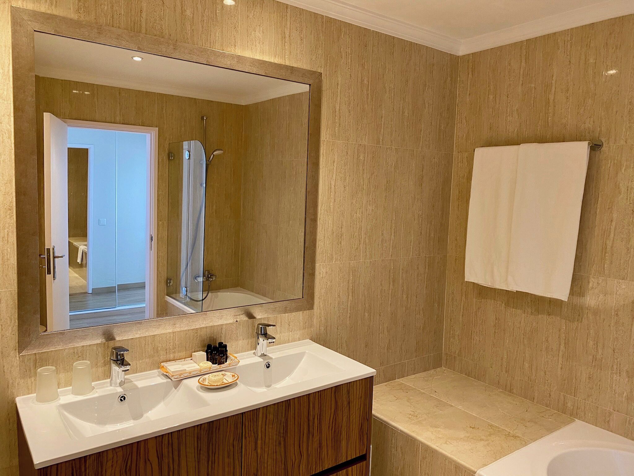 Un baño moderno con un espejo grande, dos lavamanos, una ducha y un perchero para toallas.