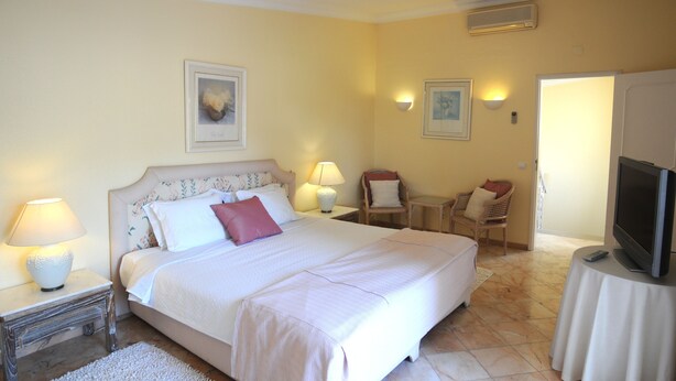 A hotel room with a bed, two bedside lamps, a chair, a television, and two framed pictures on the wall. - Vale Do Garrão Villas (Loulé)