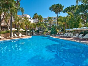 A swimming pool with lounge chairs and umbrellas, surrounded by palm trees and buildings. - Vale Do Garrão Villas (Loulé)