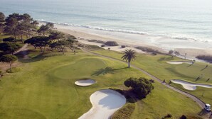 An aerial view of a golf course with sand bunkers, a palm tree, and a beach in the background. - Vale Do Garrão Villas (Loulé)